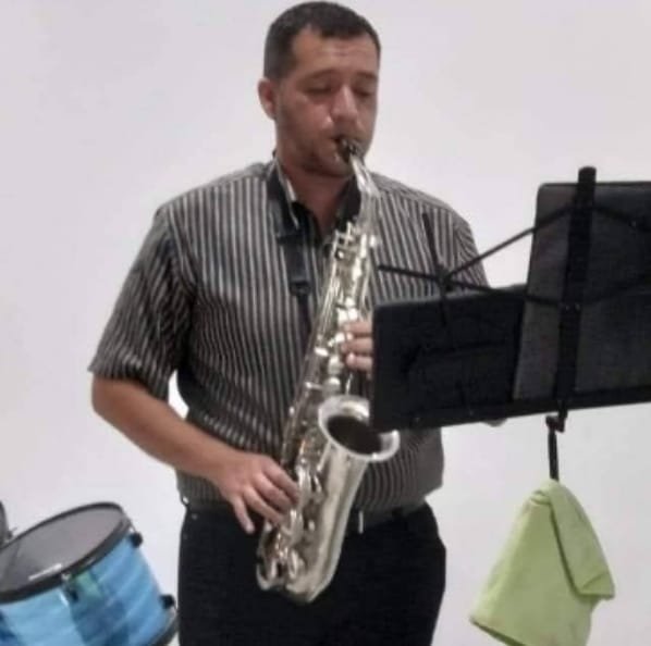 Hombre de camisa de rayas tocando el saxofón leyendo una partitura en un atril