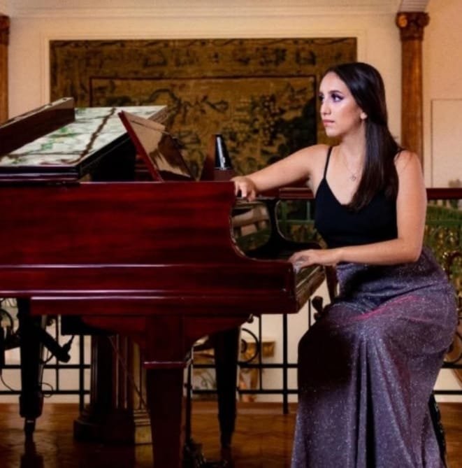 mujer de vestido negro sin mangas sentada junto a piano de cola color rojo