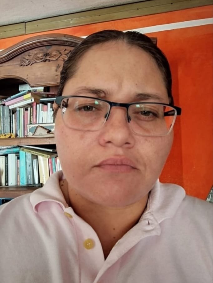 Mujer de lentes en primer plano, con libros en segundo plano