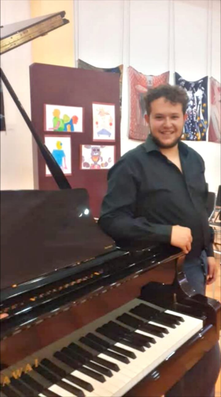 Hombre parado junto a un piano de media cola sonriendo